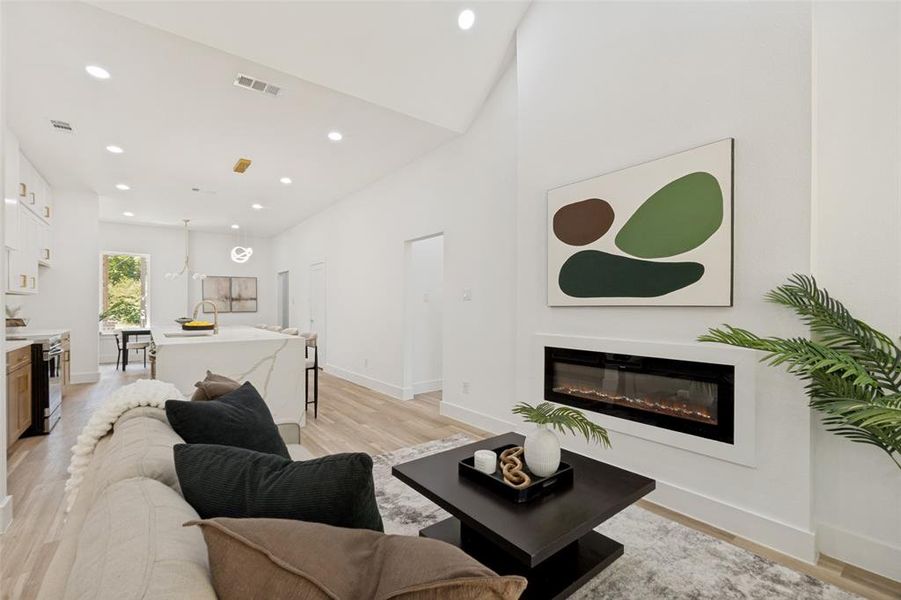Living area featuring a sleek linear electric fireplace, high vaulted ceilings, recessed lighting, and light wood-finish flooring Living area featuring a sleek linear electric fireplace, high vaulted ceilings, recessed lighting, and light wood-finish flooring