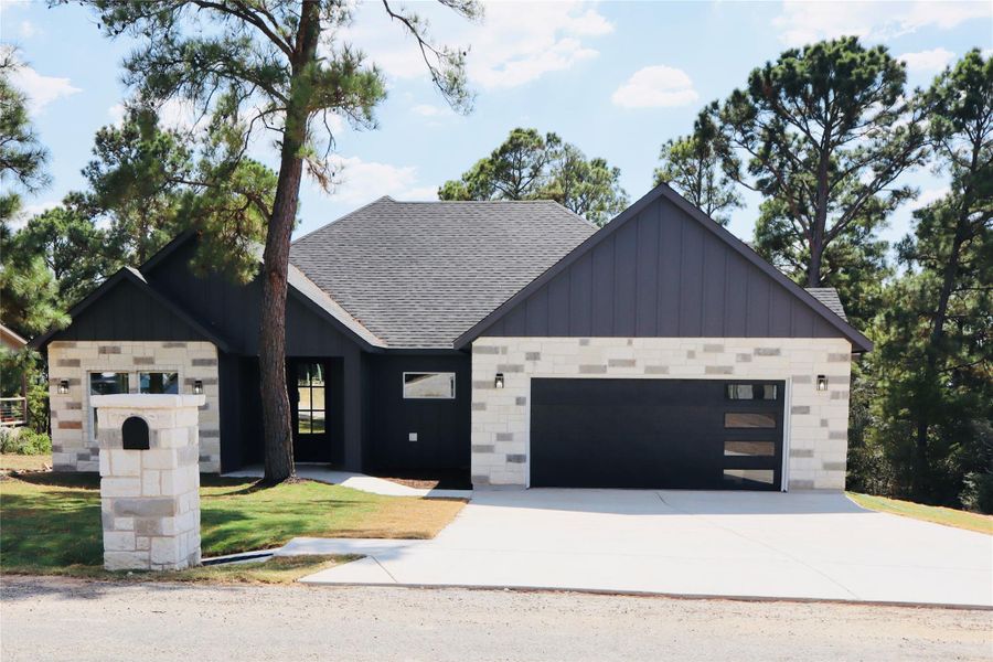 Modern farmhouse style home featuring a garage, board and batten siding, driveway, roof with shingles, and stone siding