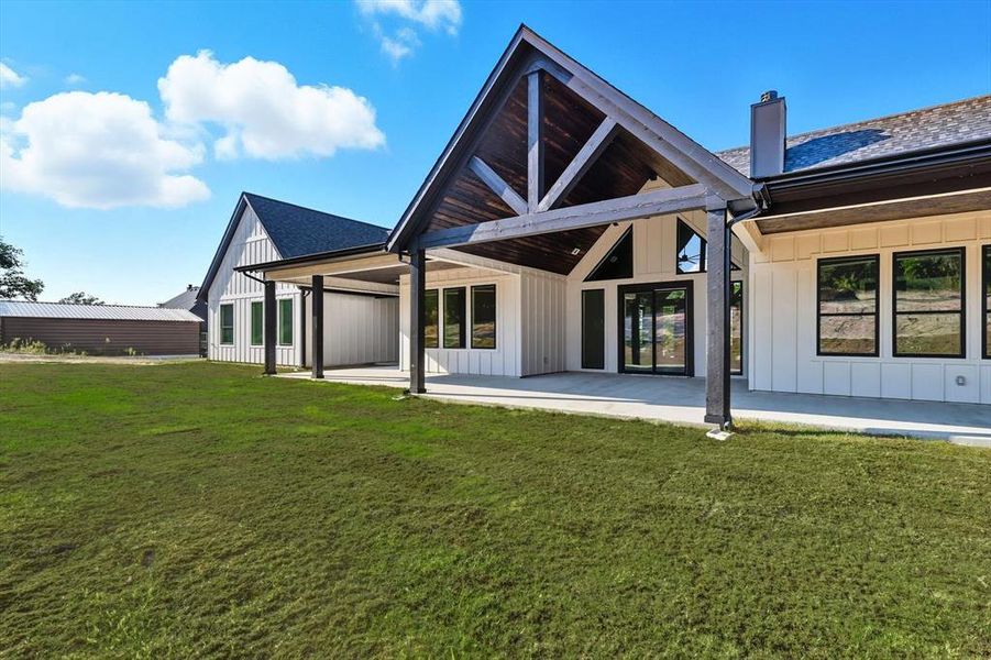 Back of house with board and batten siding, a patio area, a lawn, and a chimney Back of house with board and batten siding, a patio area, a lawn, and a chimney