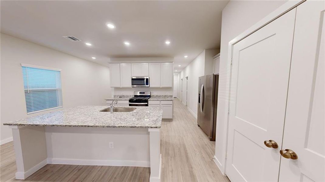 Modern kitchen with granite countertops, stainless steel appliances, and white cabinetry. Spacious layout with a central island and ample lighting.