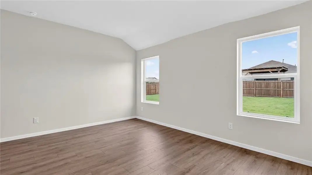 Vaulted ceiling room featuring wood-finish flooring, light neutral wall paint, and two windows providing natural light