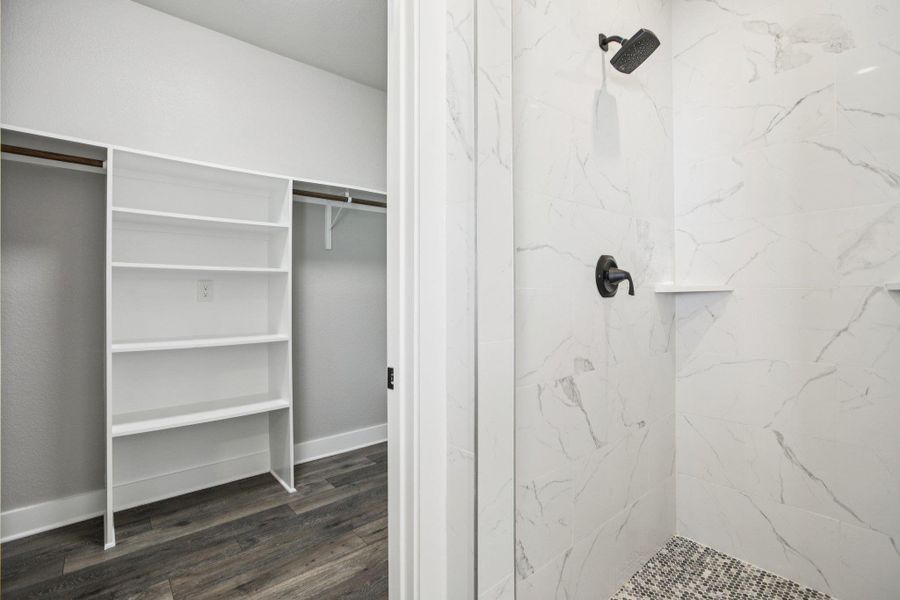 Full bath featuring a walk in closet, a marble finish shower, and dark wood finished floors