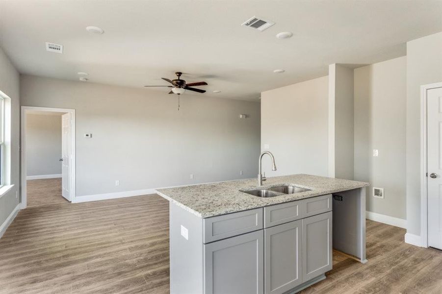Kitchen with light stone counters, gray cabinets, light wood finished floors, and a ceiling fan