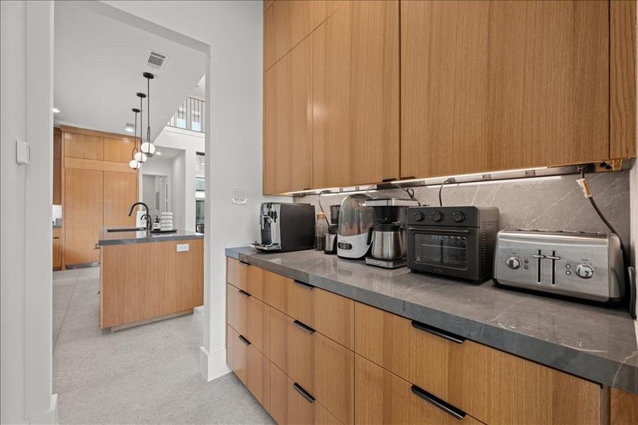 Kitchen featuring butler's pantry modern cabinets, decorative light fixtures, tasteful backsplash, and a kitchen island with sink