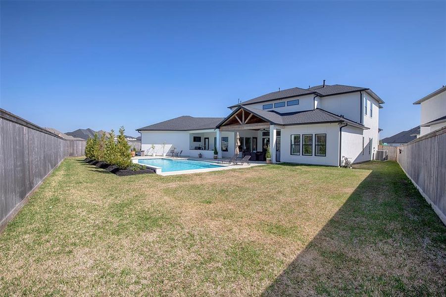 This photo features a spacious backyard with a well-maintained lawn, a modern two-story house, and a private pool. The area is enclosed by a wooden fence, providing privacy and a cozy outdoor space for relaxation and entertainment.