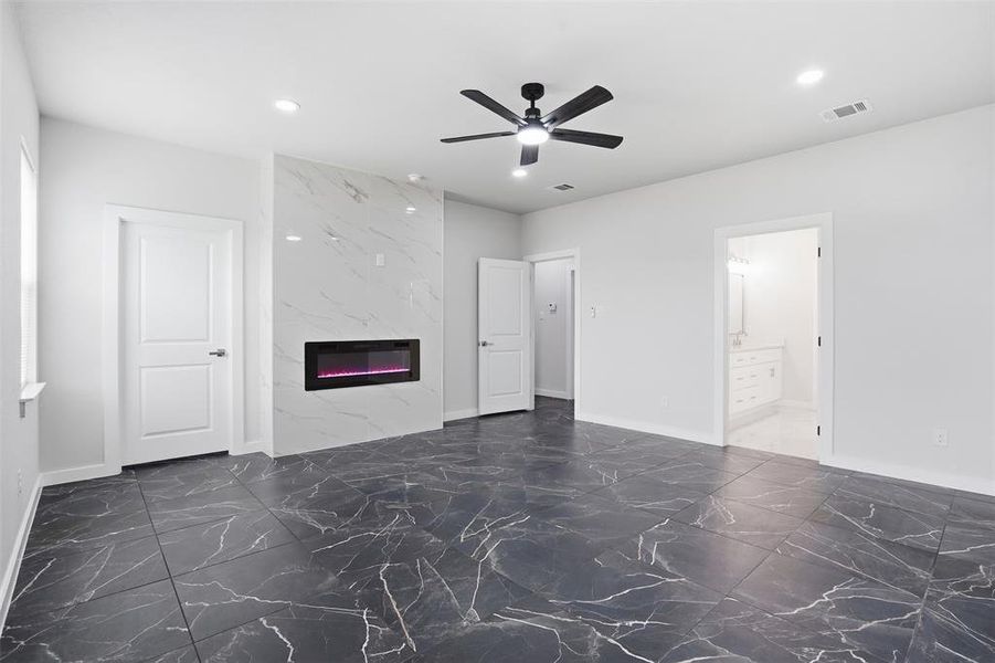 Spacious room featuring large format dark tile flooring with white veining, a built-in electric fireplace with a white marble-look surround, a ceiling fan with integrated lighting, and recessed ceiling lights