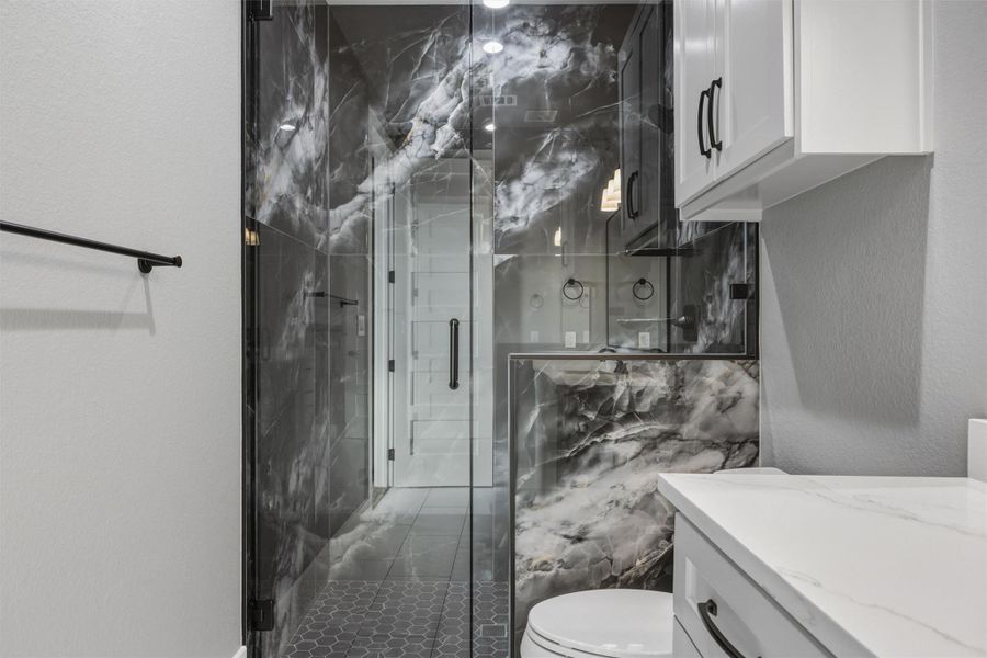 Bathroom with a textured wall, a marble finish shower, and vanity