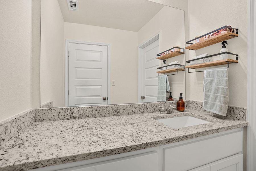 A well-lit bathroom vanity features a granite countertop and contemporary shelving.