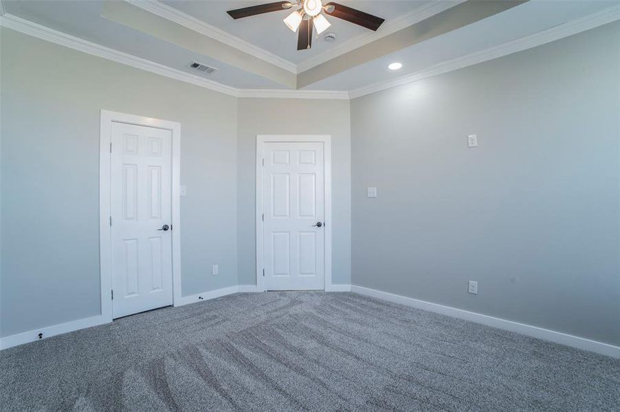 Unfurnished bedroom featuring a raised ceiling, ornamental molding, carpet floors, a ceiling fan, and recessed lighting Unfurnished bedroom featuring a raised ceiling, ornamental molding, carpet floors, a ceiling fan, and recessed lighting