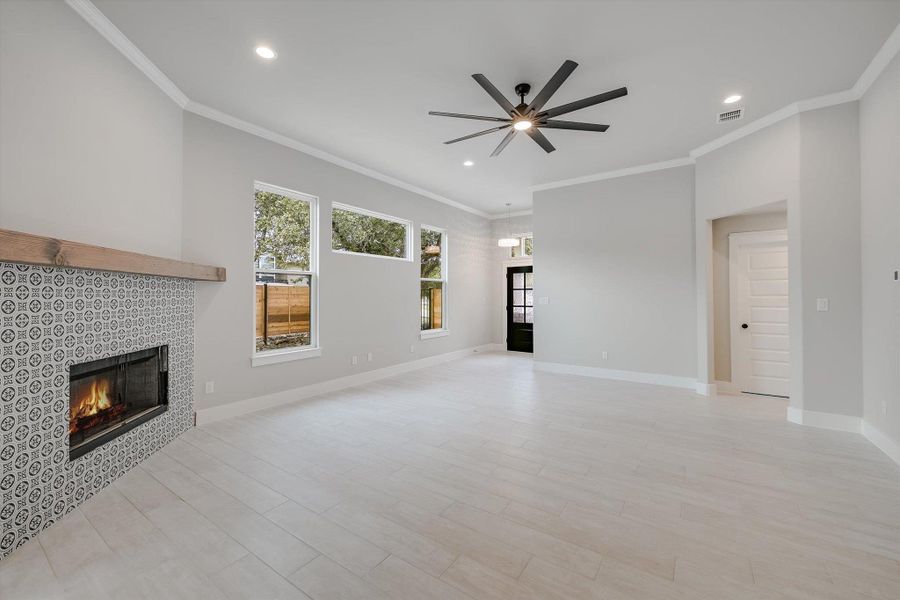 Unfurnished living room with a wealth of natural light, a tiled fireplace, visible vents, and baseboards