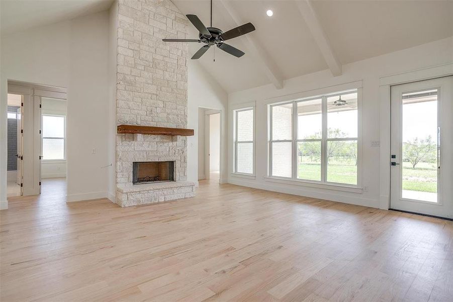 Unfurnished living room featuring a ceiling fan, healthy amount of natural light, high vaulted ceiling, light wood finished floors, and beamed ceiling