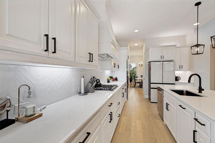Bright kitchen featuring white shaker cabinetry, quartz countertops, a herringbone tile backsplash, and light wood-finish flooring