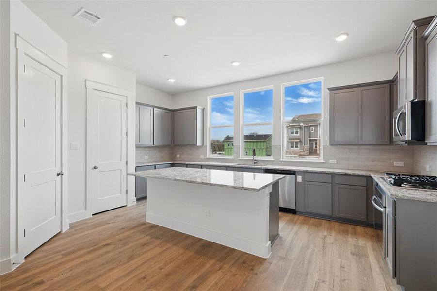 Kitchen with gray cabinets, light stone countertops, a kitchen island, light wood finished floors, and stainless steel appliances