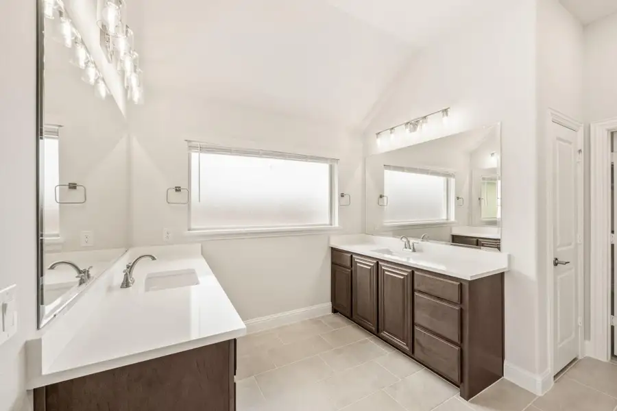 Bathroom with dual vanities, dark wood cabinets, white countertops, and vaulted ceiling with tile floors