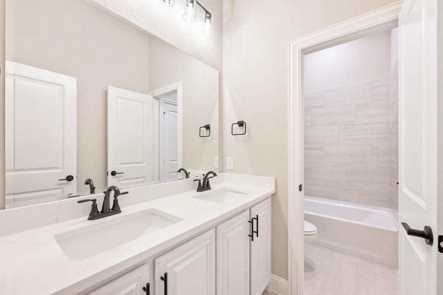 Bathroom with double sink vanity, white cabinets, and tiled shower-tub combo visible through doorway Bathroom with double sink vanity, white cabinets, and tiled shower-tub combo visible through doorway