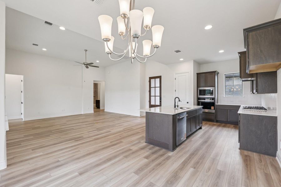 Kitchen featuring a chandelier, hanging light fixtures, dark brown cabinetry, open floor plan, and an island with sink