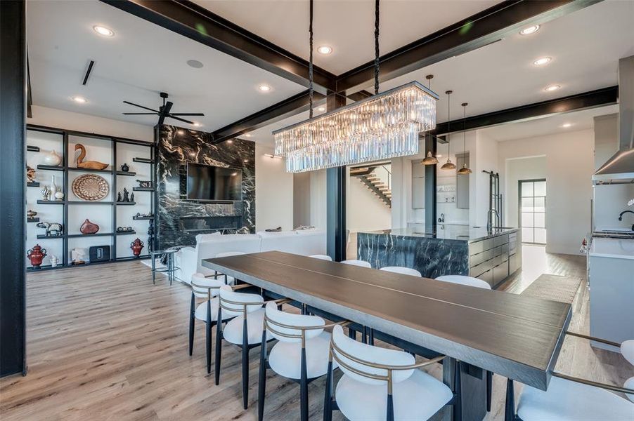 Dining room featuring ceiling fan, beamed ceiling, a premium fireplace, and light wood-type flooring