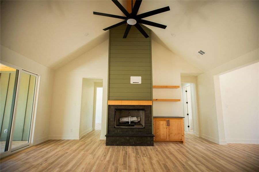 Unfurnished living room with high vaulted ceiling, visible vents, baseboards, ceiling fan, and light wood-type flooring Unfurnished living room with high vaulted ceiling, visible vents, baseboards, ceiling fan, and light wood-type flooring