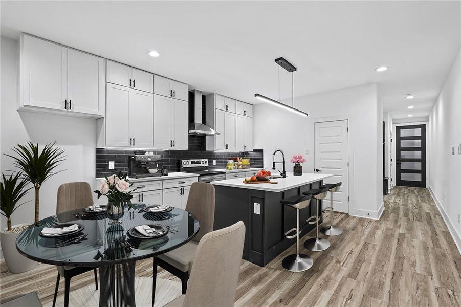 Kitchen featuring wall chimney range hood, pendant lighting, white cabinets, stainless steel range with electric cooktop, and an island with sink