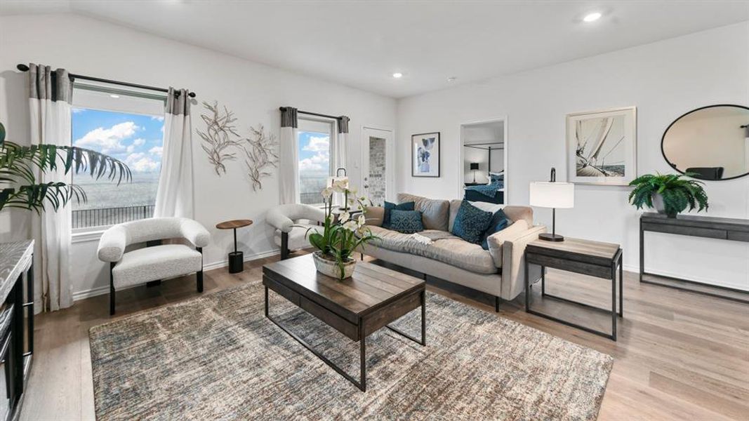 Open-concept living space with wood-finish flooring, recessed ceiling lighting, a large window, and a white interior door Open-concept living space with wood-finish flooring, recessed ceiling lighting, a large window, and a white interior door
