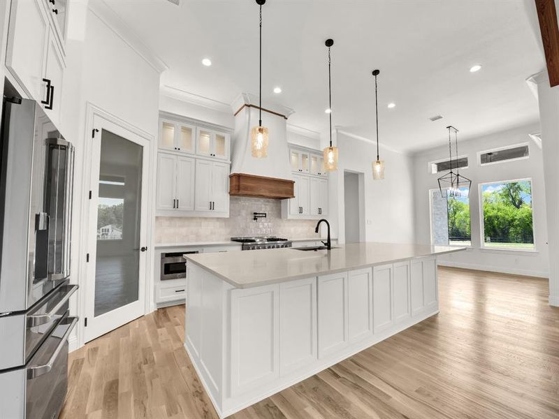 Kitchen with stainless steel fridge, a sink, custom range hood, light countertops, and backsplash Kitchen with stainless steel fridge, a sink, custom range hood, light countertops, and backsplash