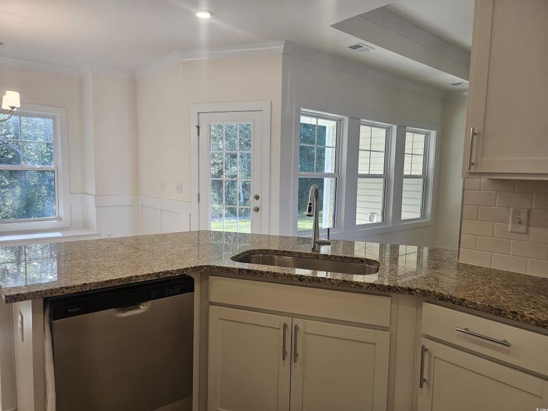 Kitchen with stainless steel dishwasher, dark stone counters, white cabinetry, ornamental molding, and backsplash Kitchen with stainless steel dishwasher, dark stone counters, white cabinetry, ornamental molding, and backsplash