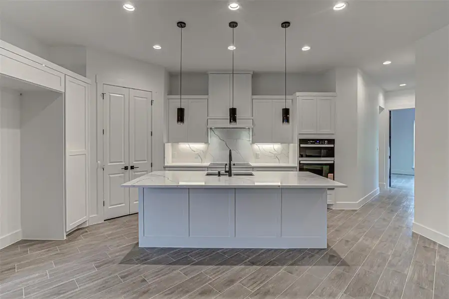 Kitchen with white cabinets, decorative light fixtures, quartz counters, a center island with sink, and recessed lighting Kitchen with white cabinets, decorative light fixtures, quartz counters, a center island with sink, and recessed lighting