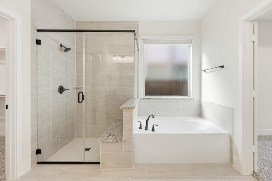 Master bathroom with glass-enclosed tile shower, soaking tub, and black fixtures on beige tile floors