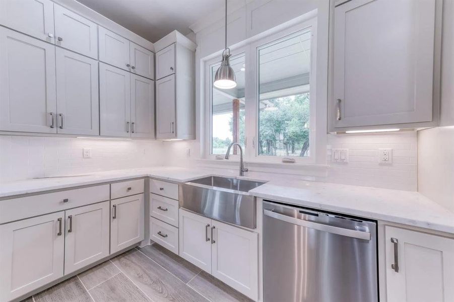 Kitchen featuring dishwasher, white cabinets, sink, light stone countertops, and pendant lighting