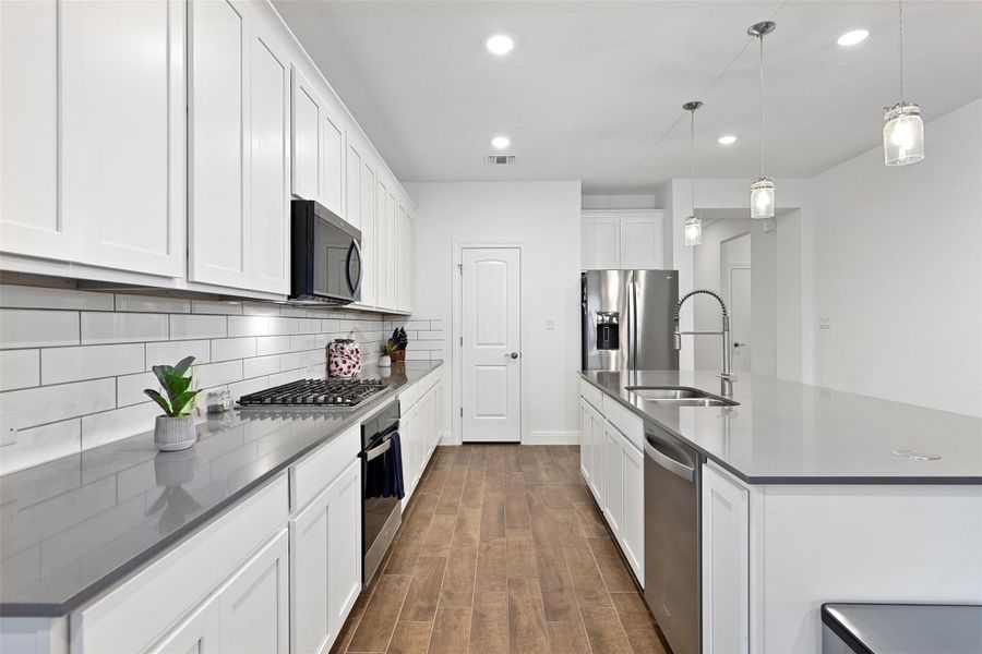Kitchen with a kitchen island with sink, pendant lighting, stainless steel appliances, white cabinetry, and dark wood finished floors
