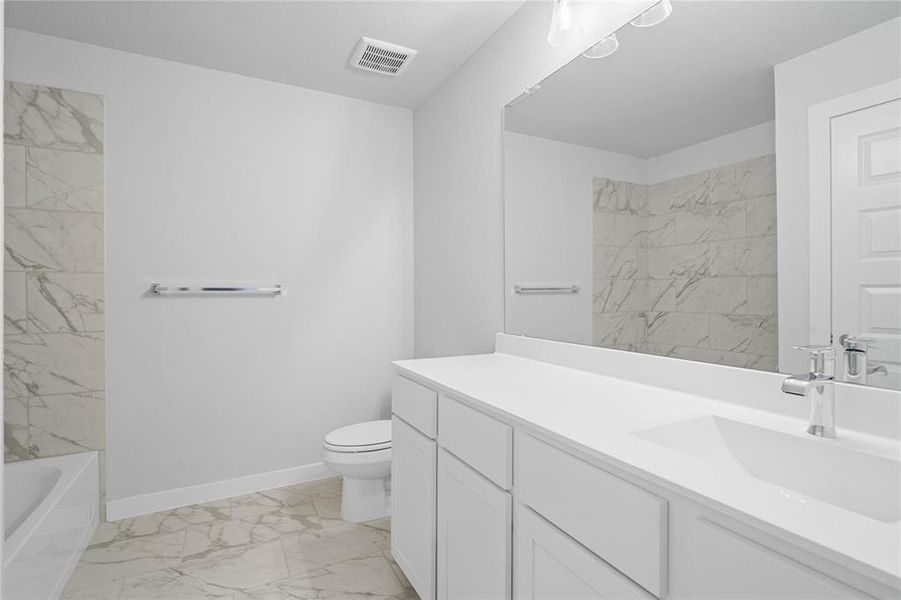 Secondary bath features tile flooring, bath/shower combo with tile surround, white stained wood cabinets, beautiful light countertops, mirror, dark, sleek fixtures and modern finishes.