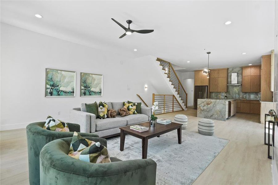 Living room featuring ceiling fan, recessed lighting, light wood-style floors, and stairs Living room featuring ceiling fan, recessed lighting, light wood-style floors, and stairs