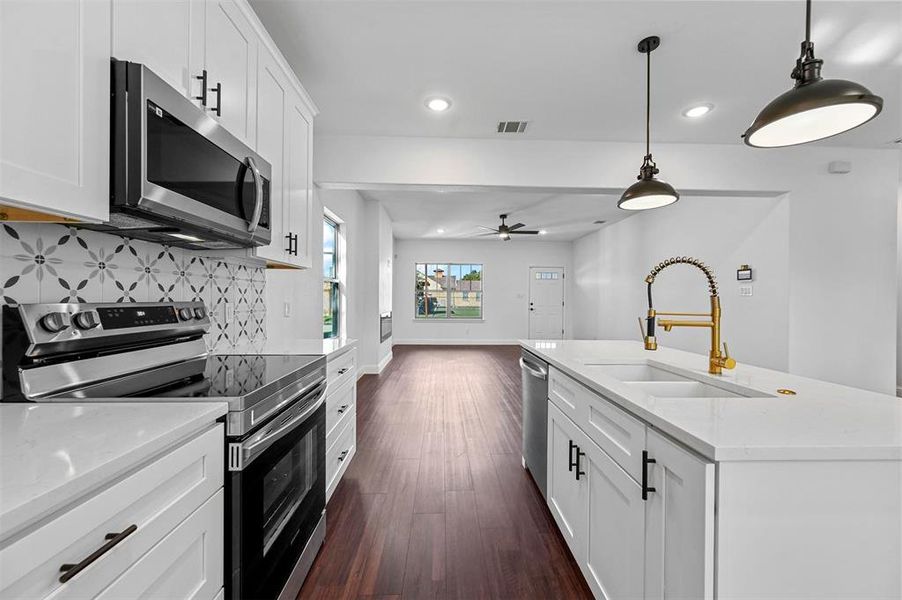 Kitchen featuring white cabinets, stainless steel appliances, a kitchen island with sink, and sink