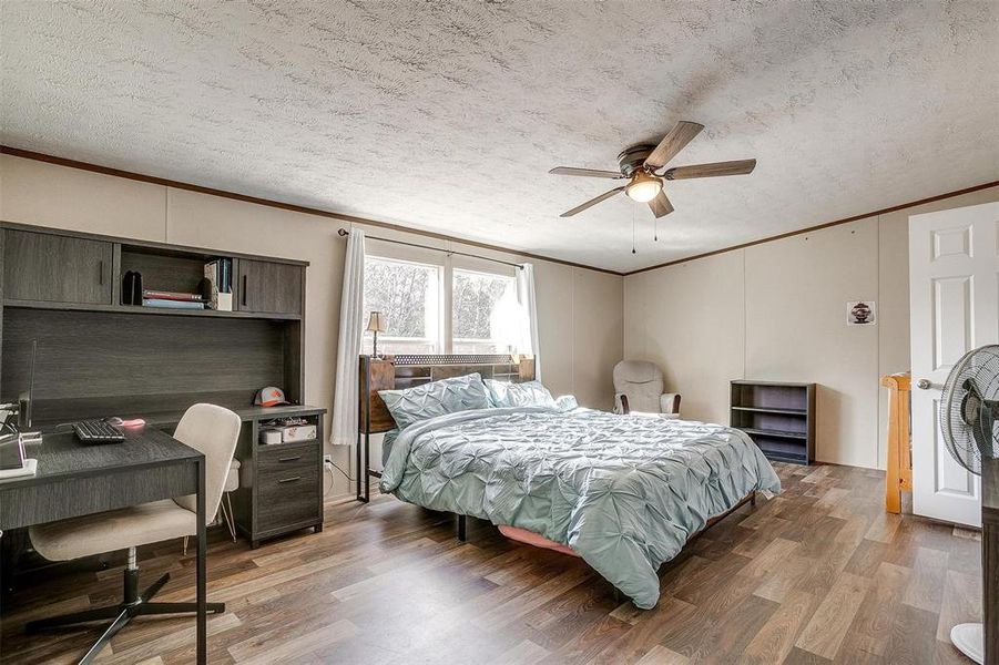 Bedroom featuring dark wood-type flooring, ceiling fan, ornamental molding, and a textured ceiling