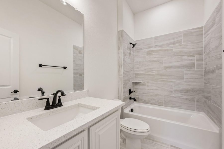 Bathroom with white quartz vanity, black fixtures, and tiled tub-shower combo with gray stone-look tile Bathroom with white quartz vanity, black fixtures, and tiled tub-shower combo with gray stone-look tile