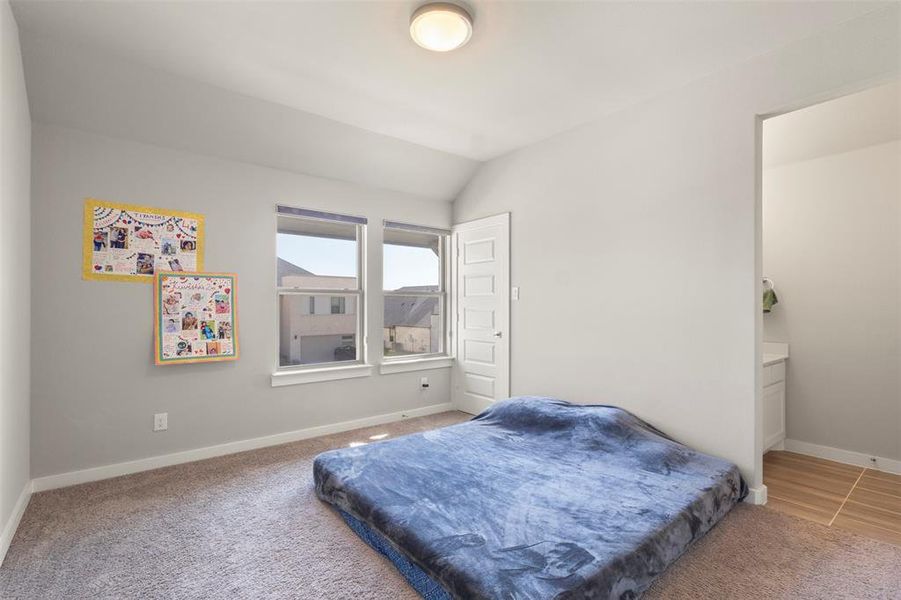 Bedroom with light colored carpet, vaulted ceiling, and ensuite bathroom