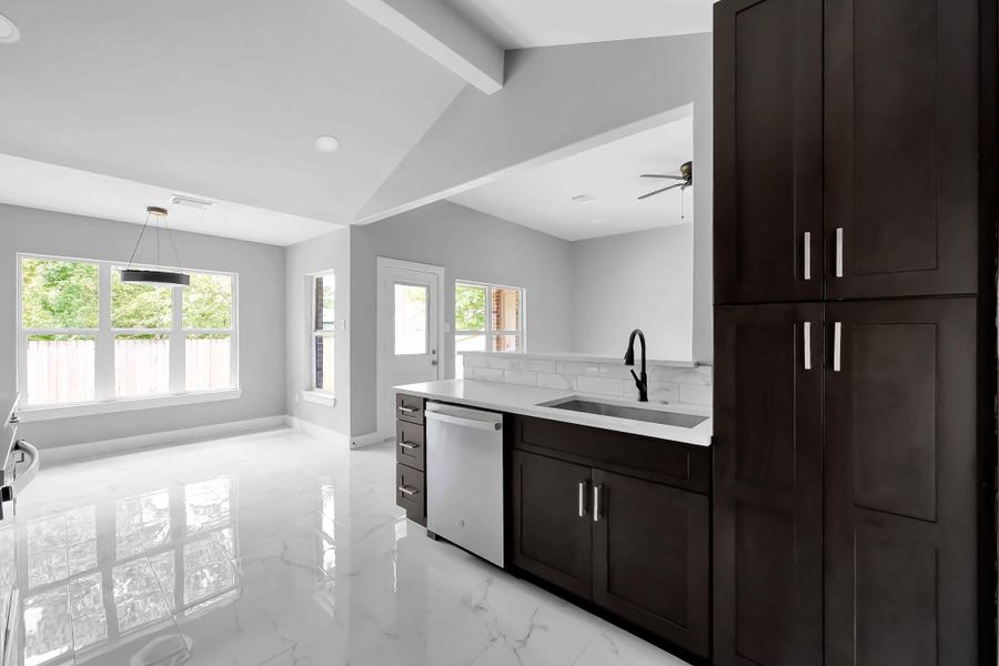 This photo showcases a modern, open-concept kitchen and dining area with sleek dark cabinets, a white countertop, and a stylish black faucet. The space features large windows for natural light, a glossy tile floor, and a contemporary pendant light, creating a bright and inviting atmosphere. This photo showcases a modern, open-concept kitchen and dining area with sleek dark cabinets, a white countertop, and a stylish black faucet. The space features large windows for natural light, a glossy tile floor, and a contemporary pendant light, creating a bright and inviting atmosphere.