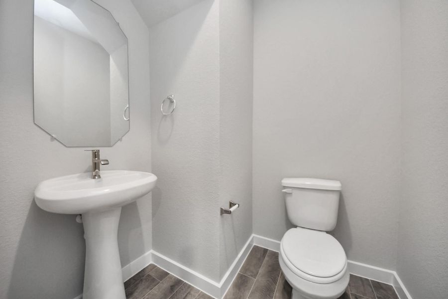This half bathroom features a stylish pedestal sink, modern hardware, and bright recessedlighting, creating a sleek and inviting space.