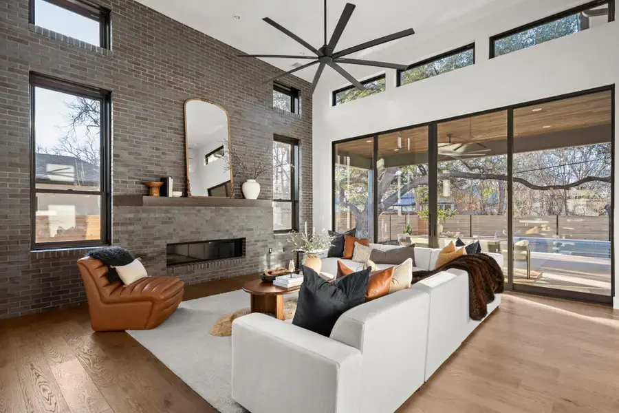 Living room featuring a towering ceiling, brick wall, a brick fireplace, wood finished floors, and healthy amount of natural light