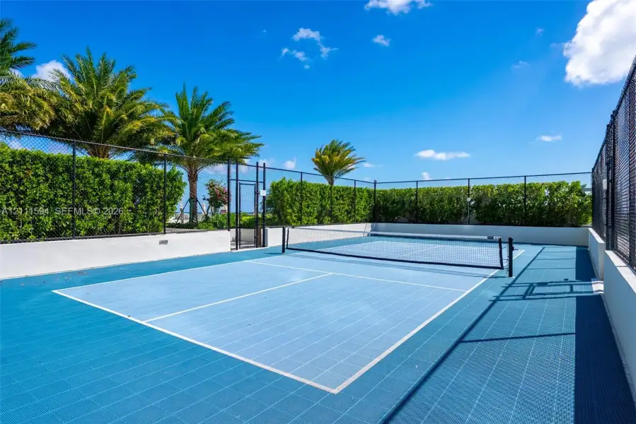 Private pickleball court featuring a blue modular surface, perimeter chain-link fencing, and manicured hedge privacy screening Private pickleball court featuring a blue modular surface, perimeter chain-link fencing, and manicured hedge privacy screening