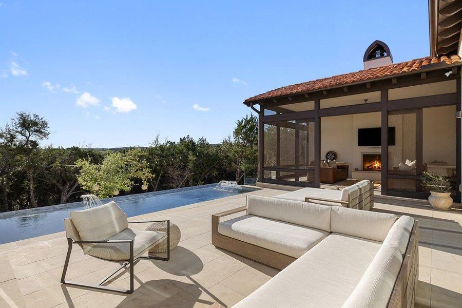 View of swimming pool with a sunroom, patio surround, an infinity pool, and an outdoor living space with a fireplace