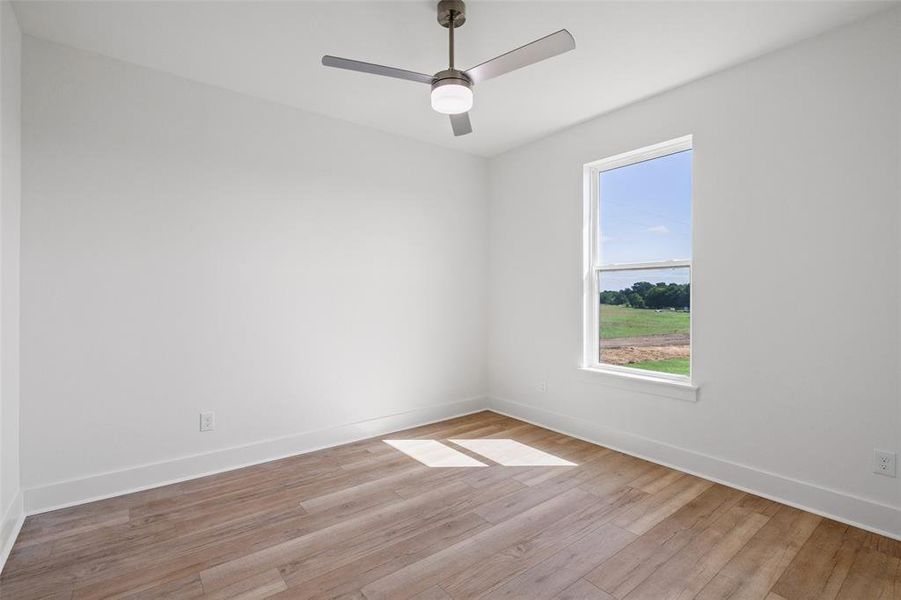 Room featuring wood-finish flooring, a contemporary ceiling fan with integrated lighting, and a window framing a pastoral landscape