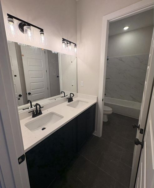 Bathroom with double vanity, dark tile patterned flooring, and bathtub / shower combination