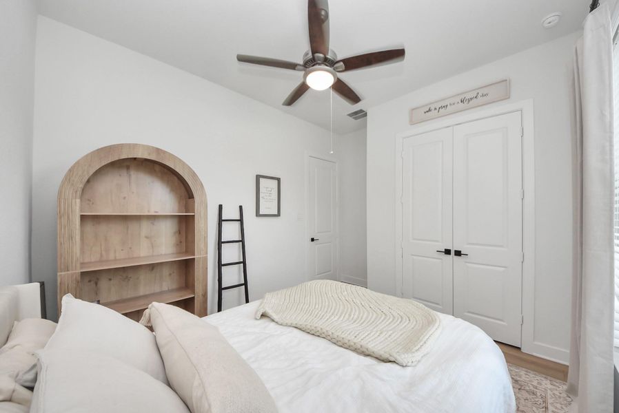Cozy bedroom featuring a stylish ceiling fan, built-in shelving, and a spacious closet with double doors.
