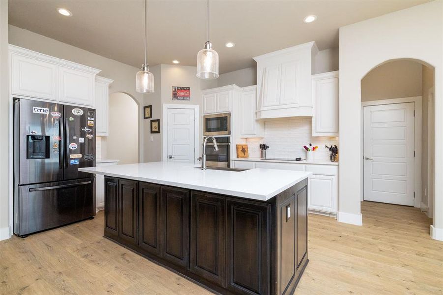 Kitchen with arched walkways, stainless steel appliances, dark brown cabinetry, decorative backsplash, and an island with sink