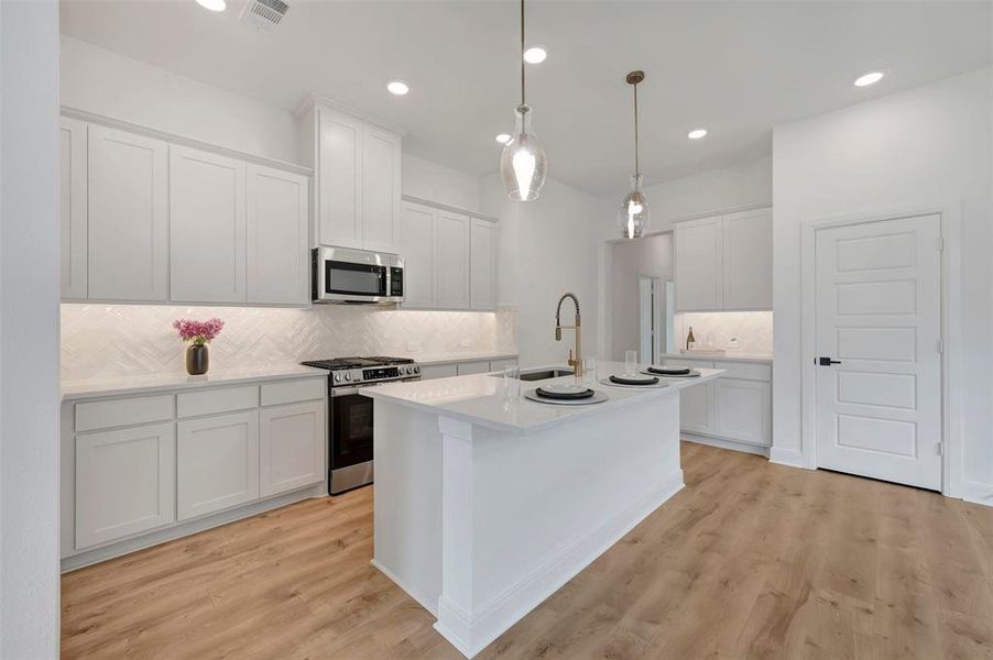 Open-concept kitchen featuring an island with seating, pendant lighting, white shaker cabinetry, stainless steel appliances, and wood-finish flooring