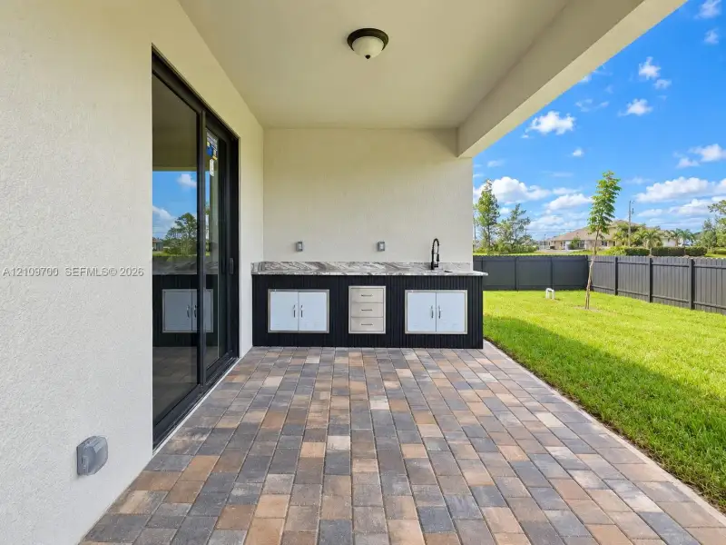 Covered outdoor patio featuring paver flooring, a built-in wet bar with cabinetry, stainless steel drawers, a stone-finish countertop, and a gooseneck faucet