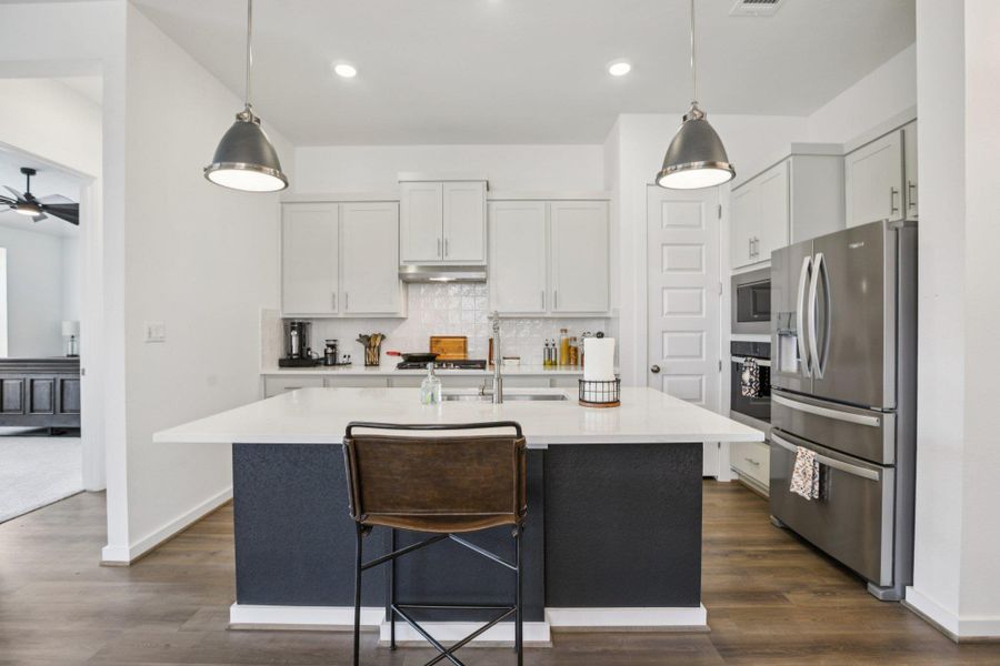 Kitchen with stainless steel appliances, hanging light fixtures, backsplash, a center island with sink, and dark wood finished floors Kitchen with stainless steel appliances, hanging light fixtures, backsplash, a center island with sink, and dark wood finished floors