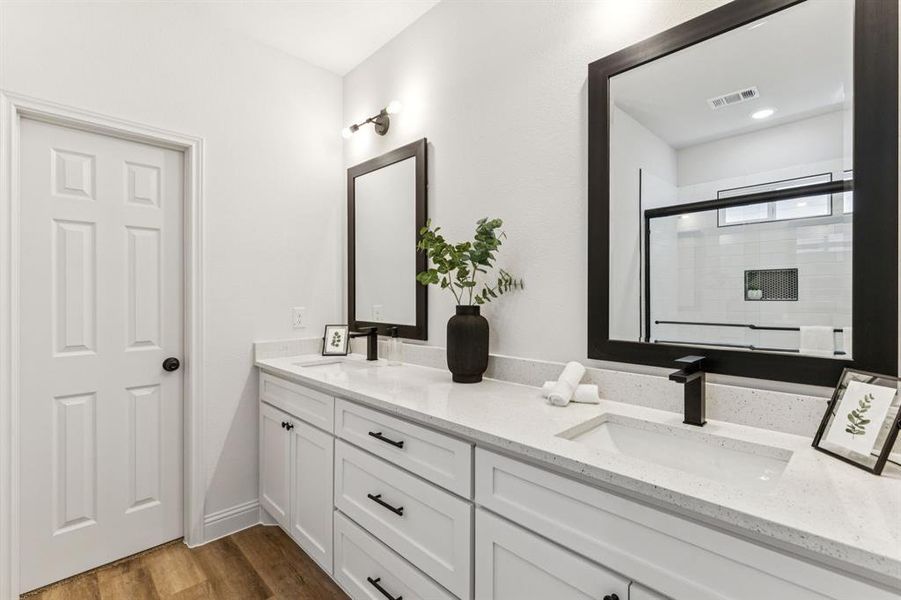 Bathroom with a shower stall, double vanity, and dark wood-type flooring