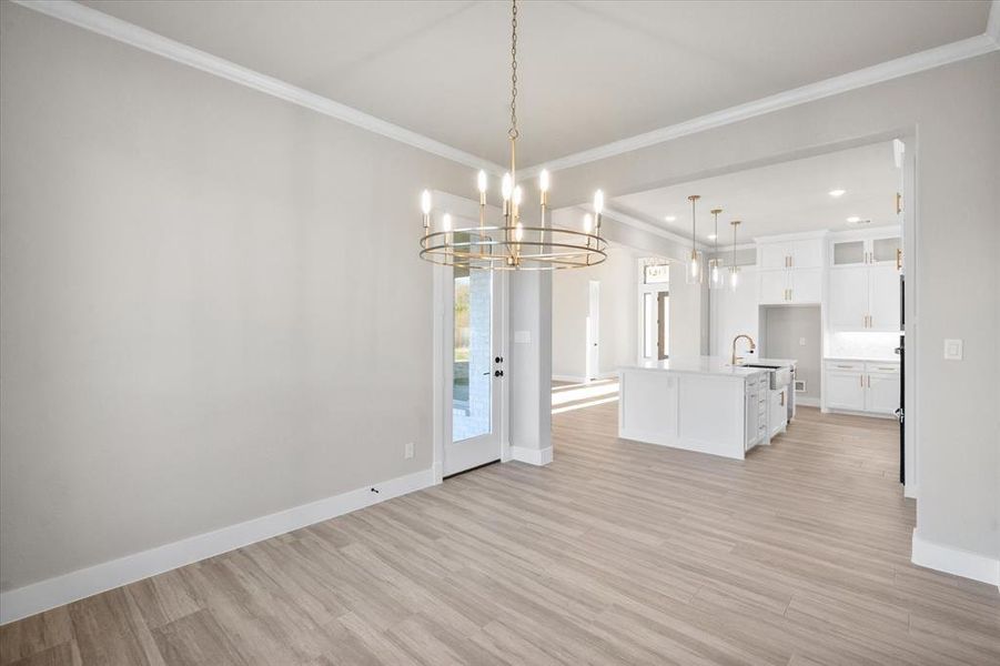 Kitchen featuring a kitchen island with sink, pendant lighting, a notable chandelier, white cabinets, and light hardwood / wood-style floors